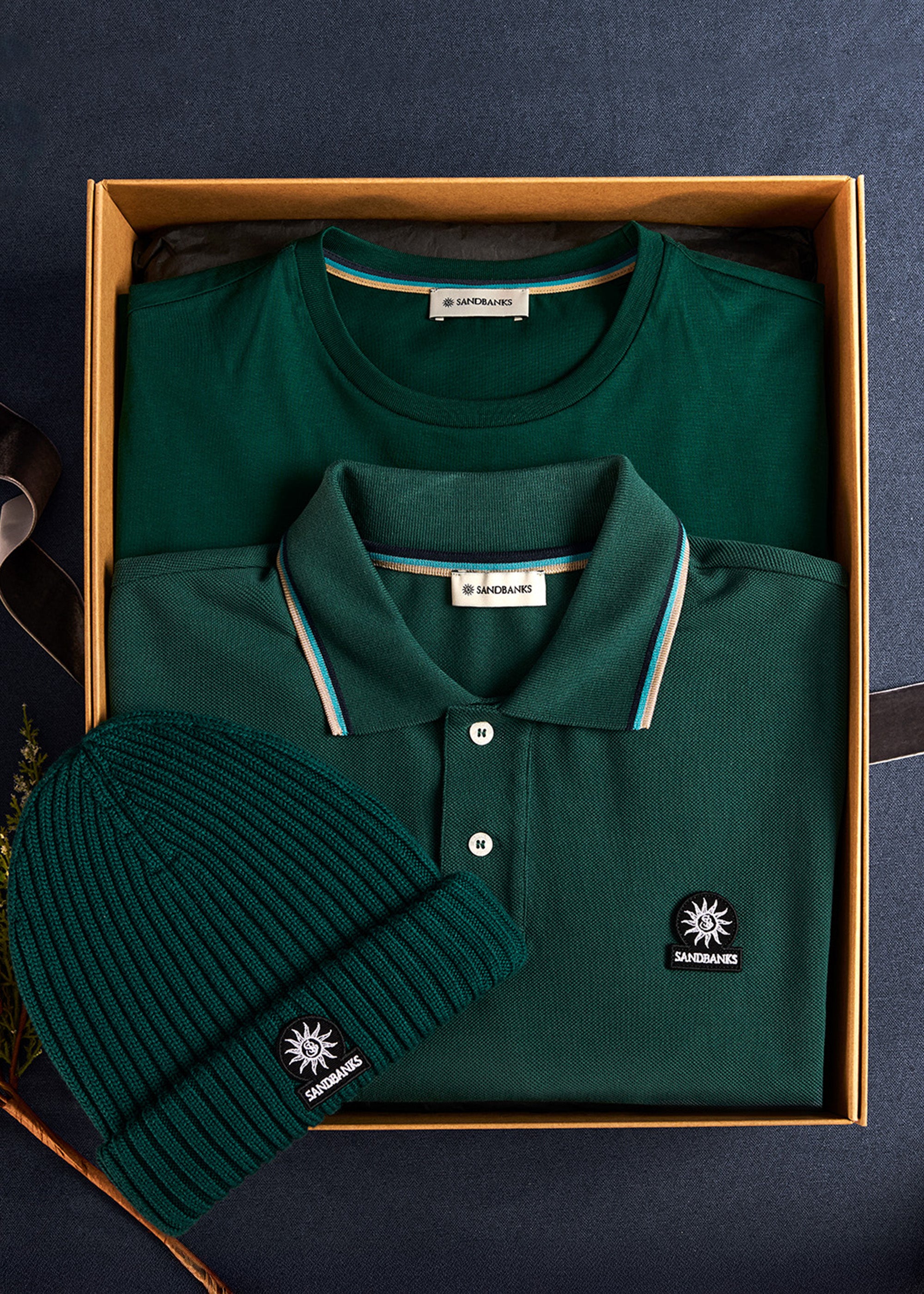 Green polo shirt, beanie, and box with brand logo on a dark blue background