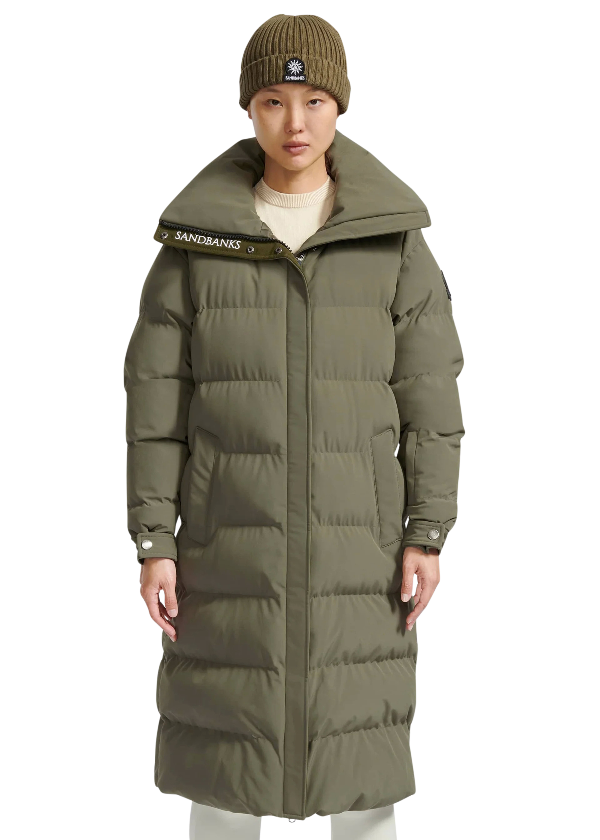 Person wearing a long green puffer coat with a brand logo on a white background