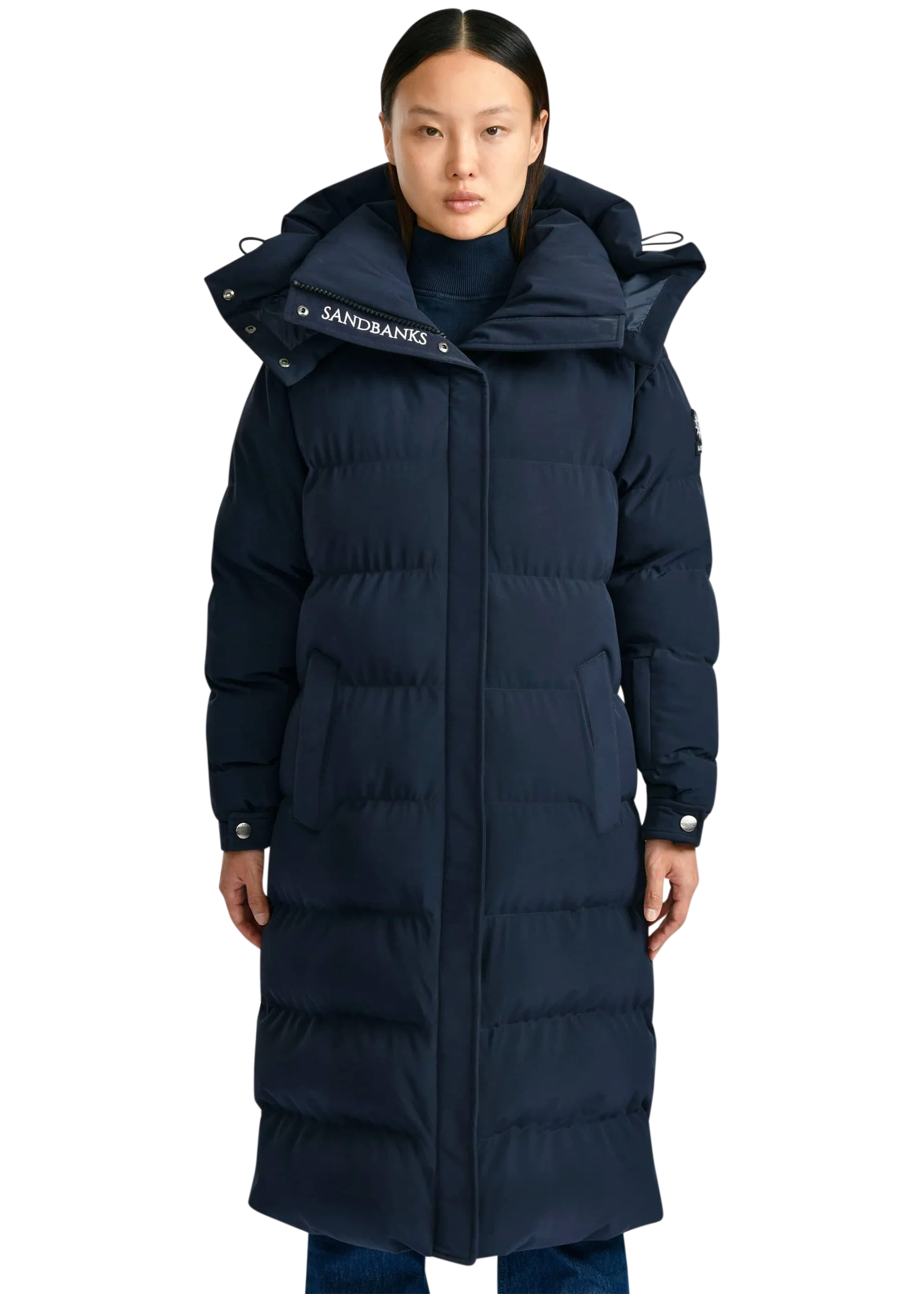 Person wearing a long navy blue puffer coat with a brand logo on a white background