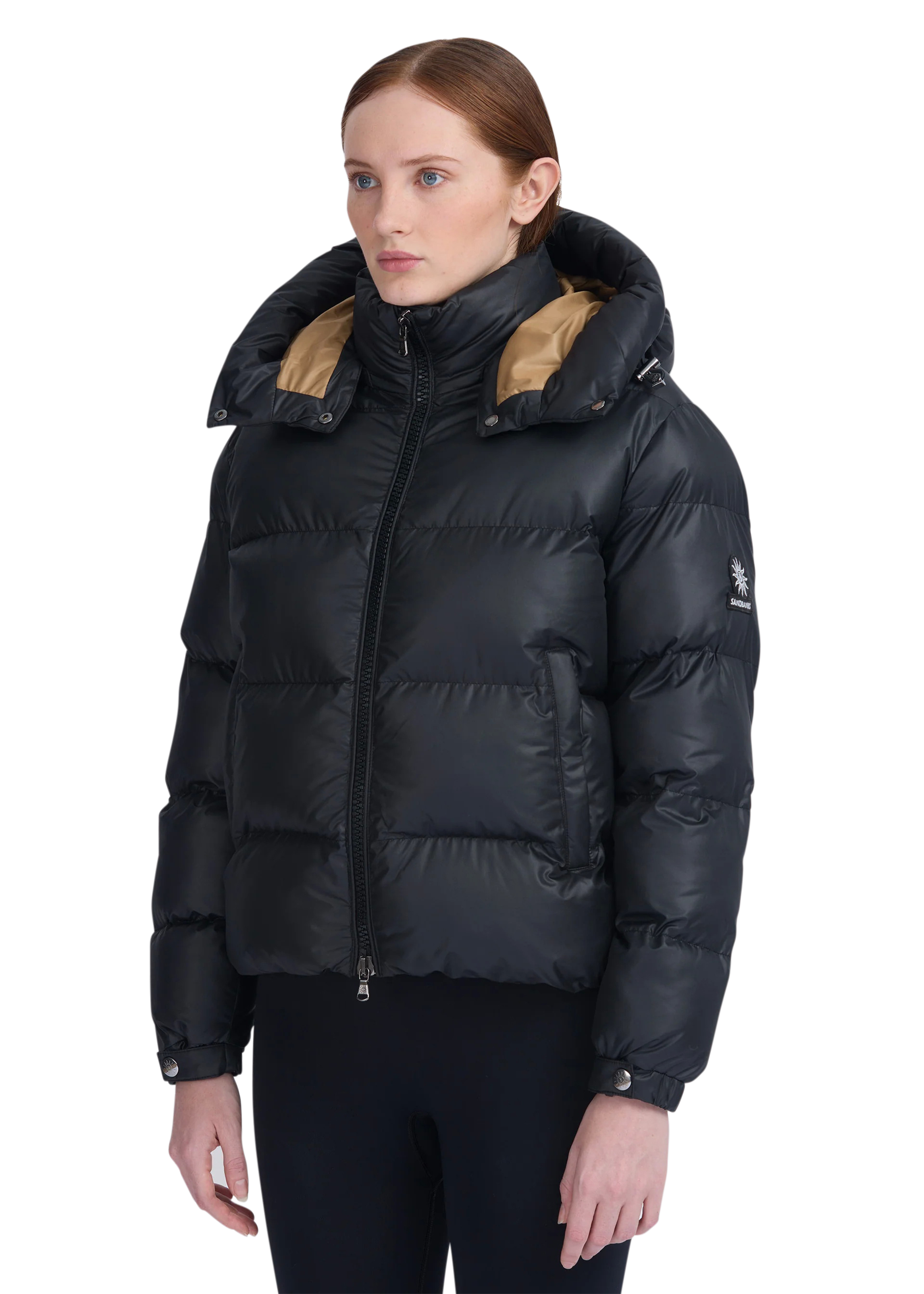 Woman wearing a black puffer jacket with beige lining on a white background