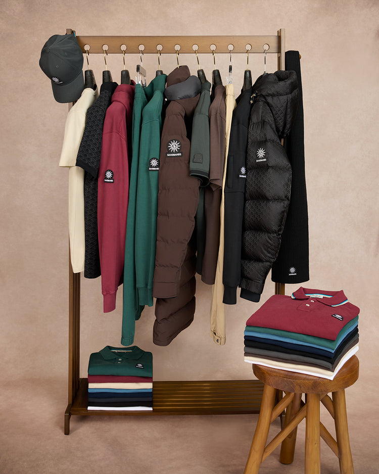 Clothing rack with various jackets and a stool with folded shirts against a beige wall.