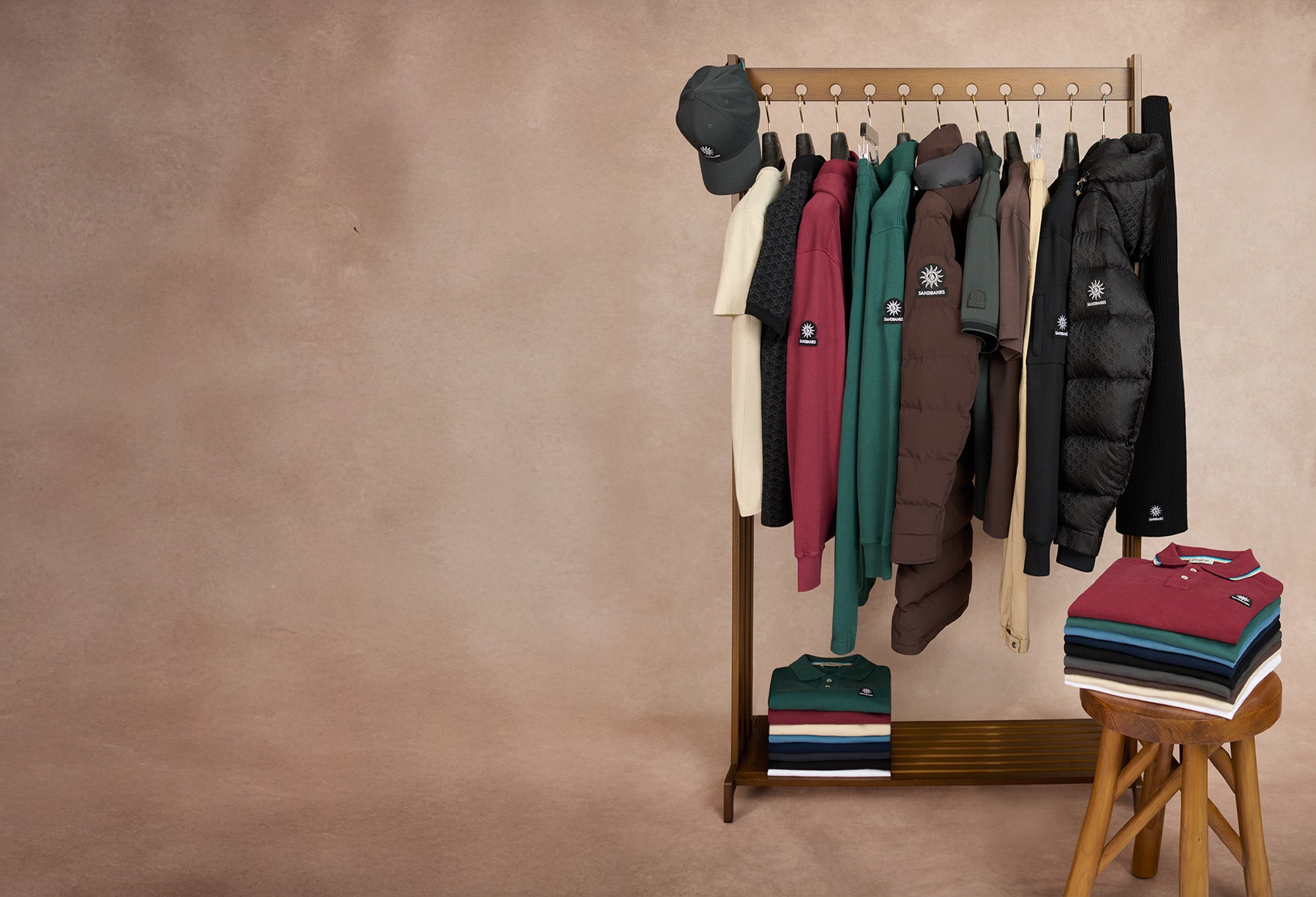 Clothing rack with jackets, a hat, and a bag against a brown wall.