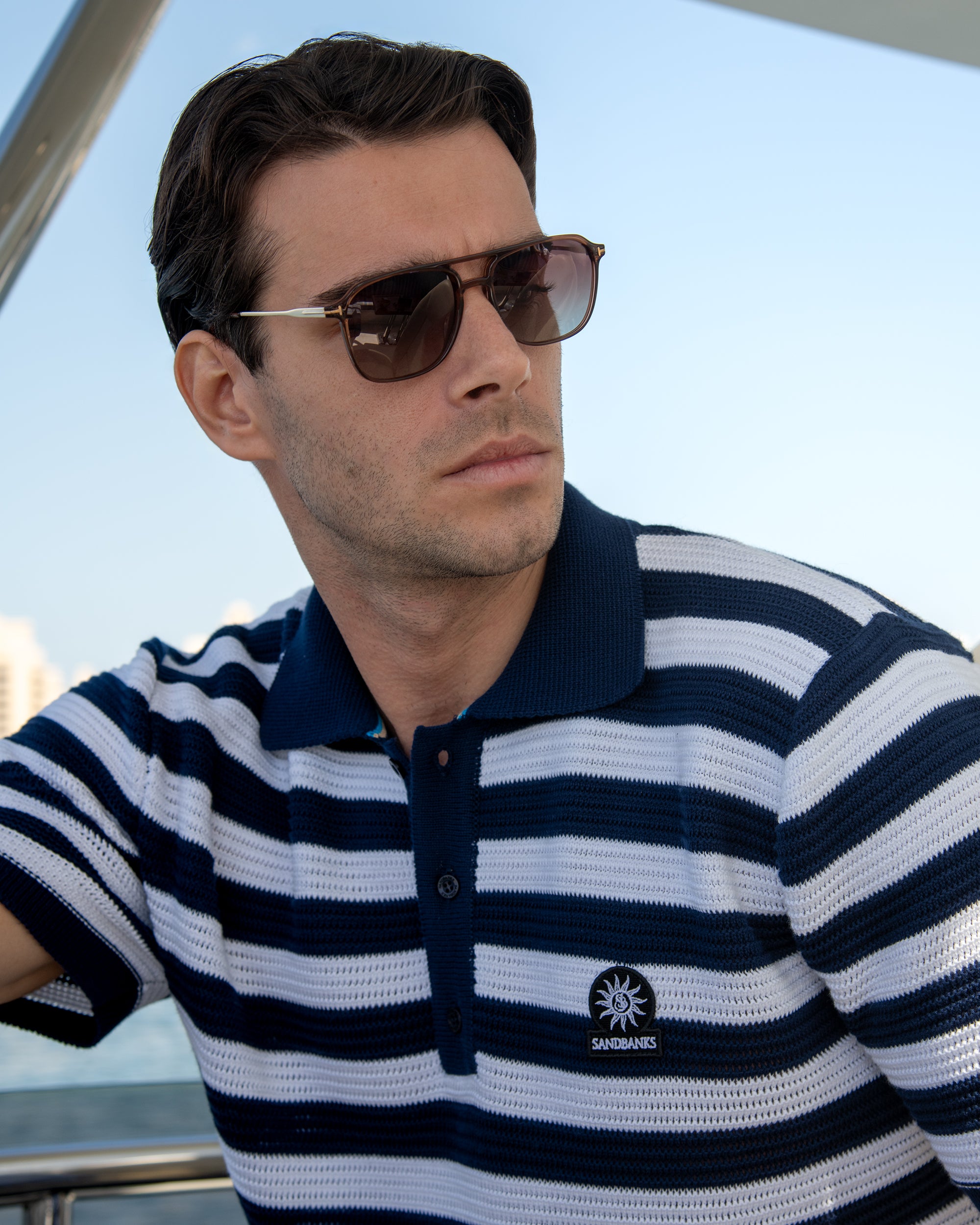 Man wearing a navy and white striped polo shirt with sunglasses on a boat.