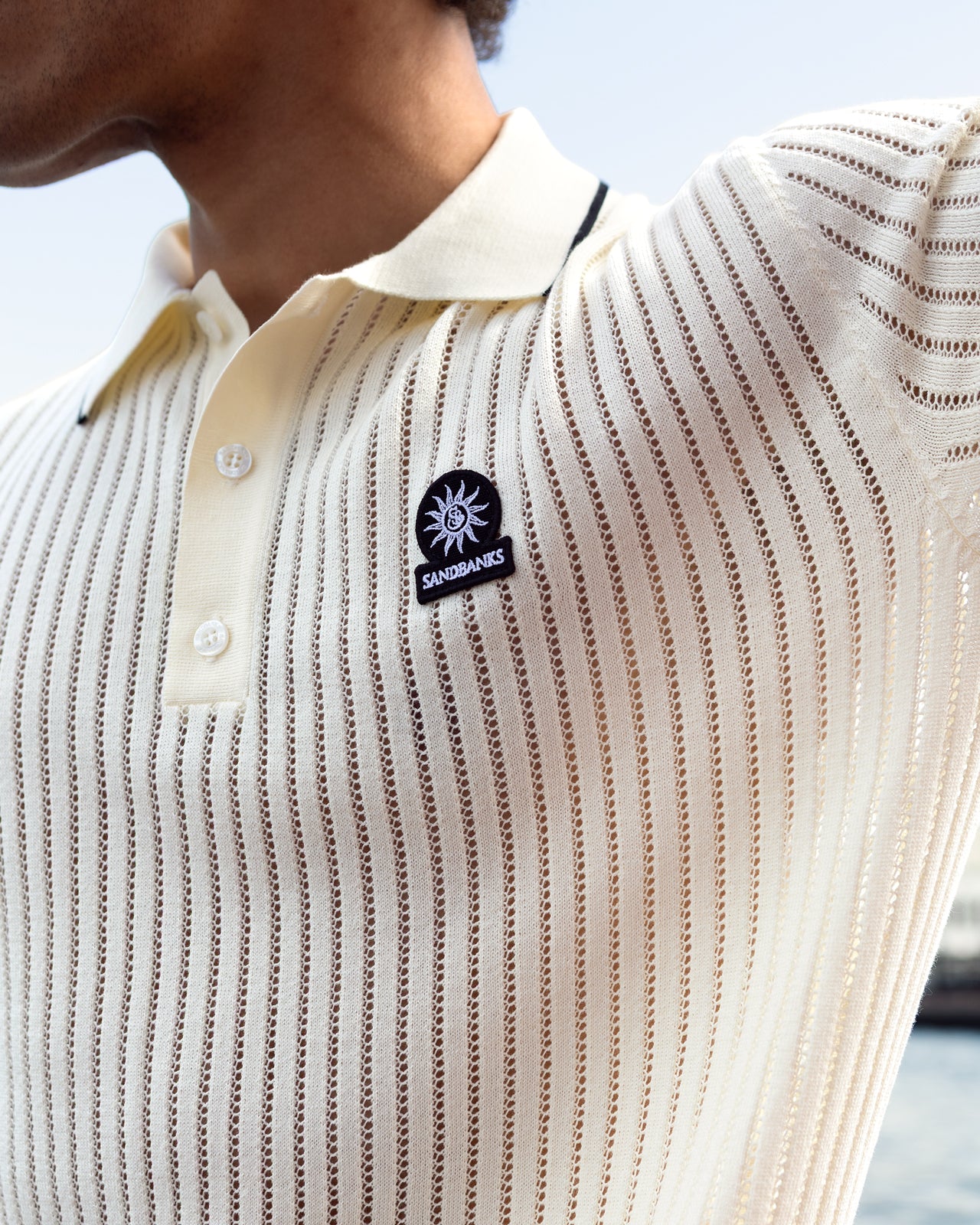 Close-up of a person wearing a textured beige shirt with a logo on the chest.