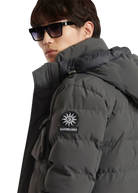 Person wearing a dark gray puffer jacket with a brand logo on a white background