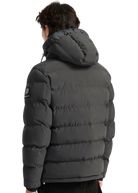 Person wearing a dark gray puffer jacket with a brand logo on the back, standing against a white background.