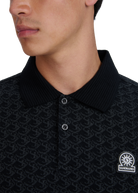 Close-up of a model wearing a black patterned polo shirt with a brand logo on a white background