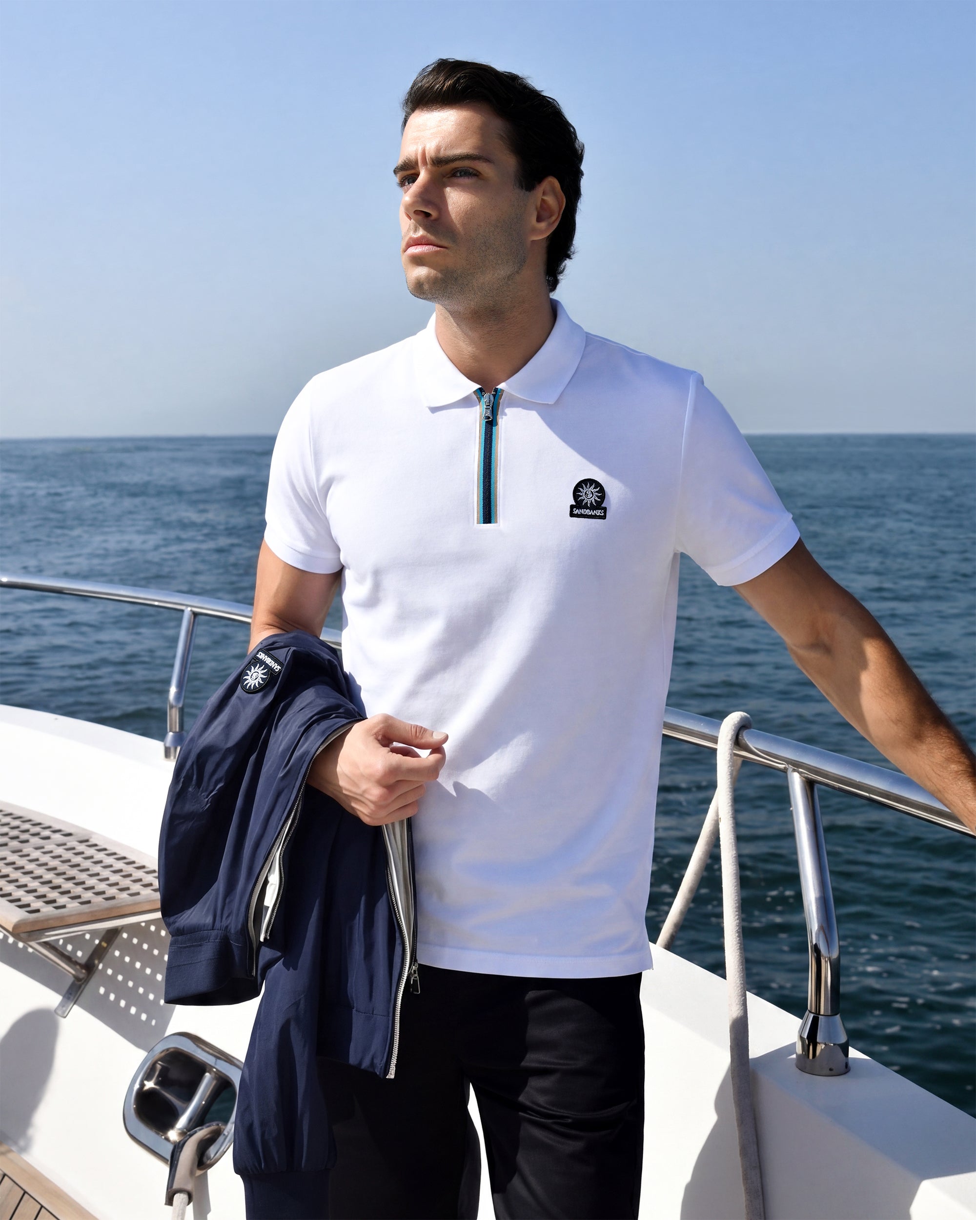 Man wearing a white polo shirt with a logo on a boat with ocean and sky background