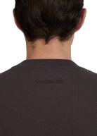 Back view of a model wearing a brown t-shirt with 'Sandbanks' branding.