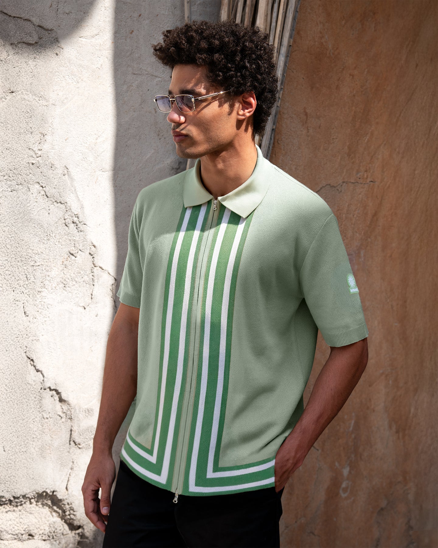 Man wearing a green and white striped polo shirt against a textured wall.