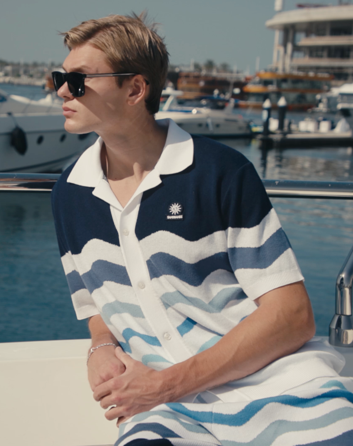 Man wearing a blue and white striped polo shirt with a marina background