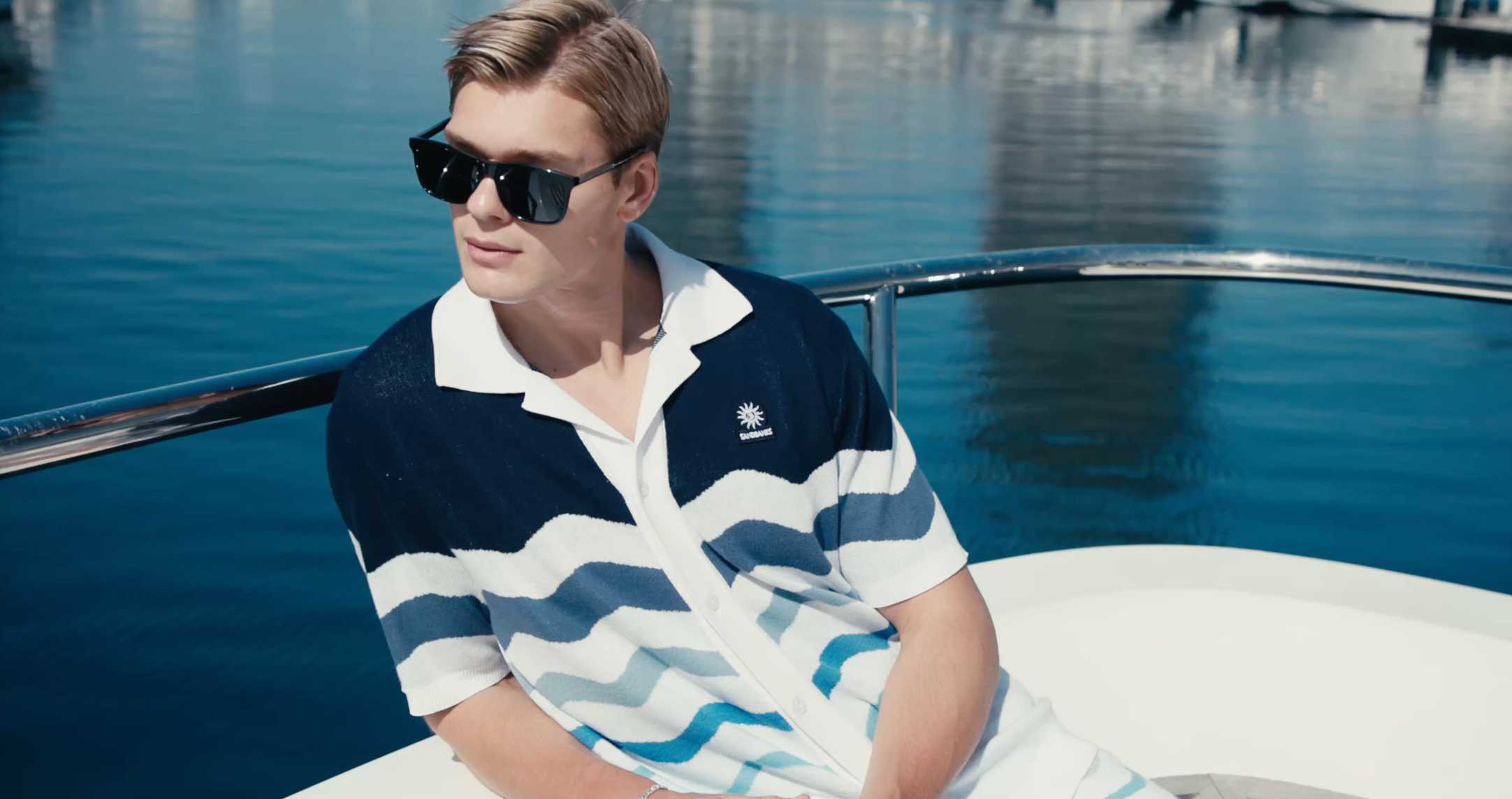 Man wearing a patterned shirt and sunglasses on a boat with water in the background
