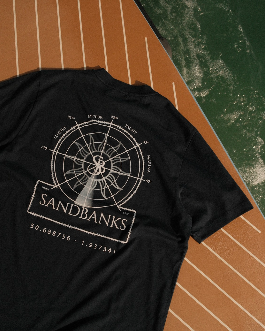 Black t-shirt with 'Sandbanks' design on a wooden deck with water in the background