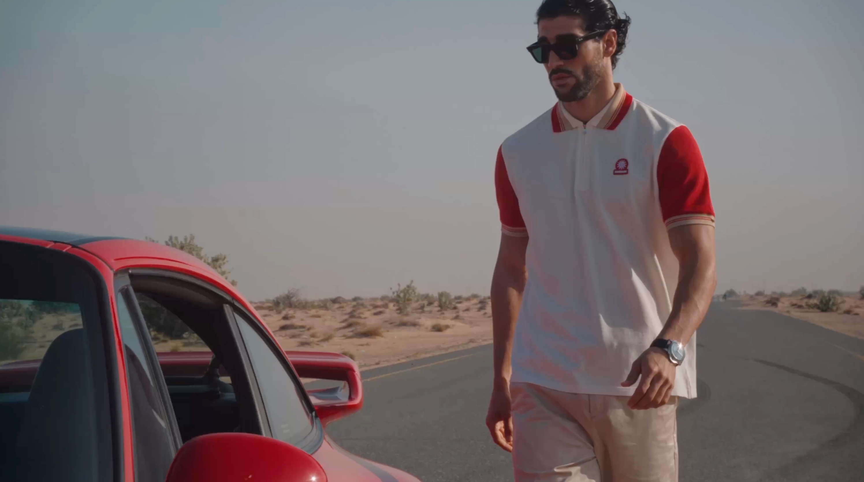 Man standing next to a red car in a desert setting