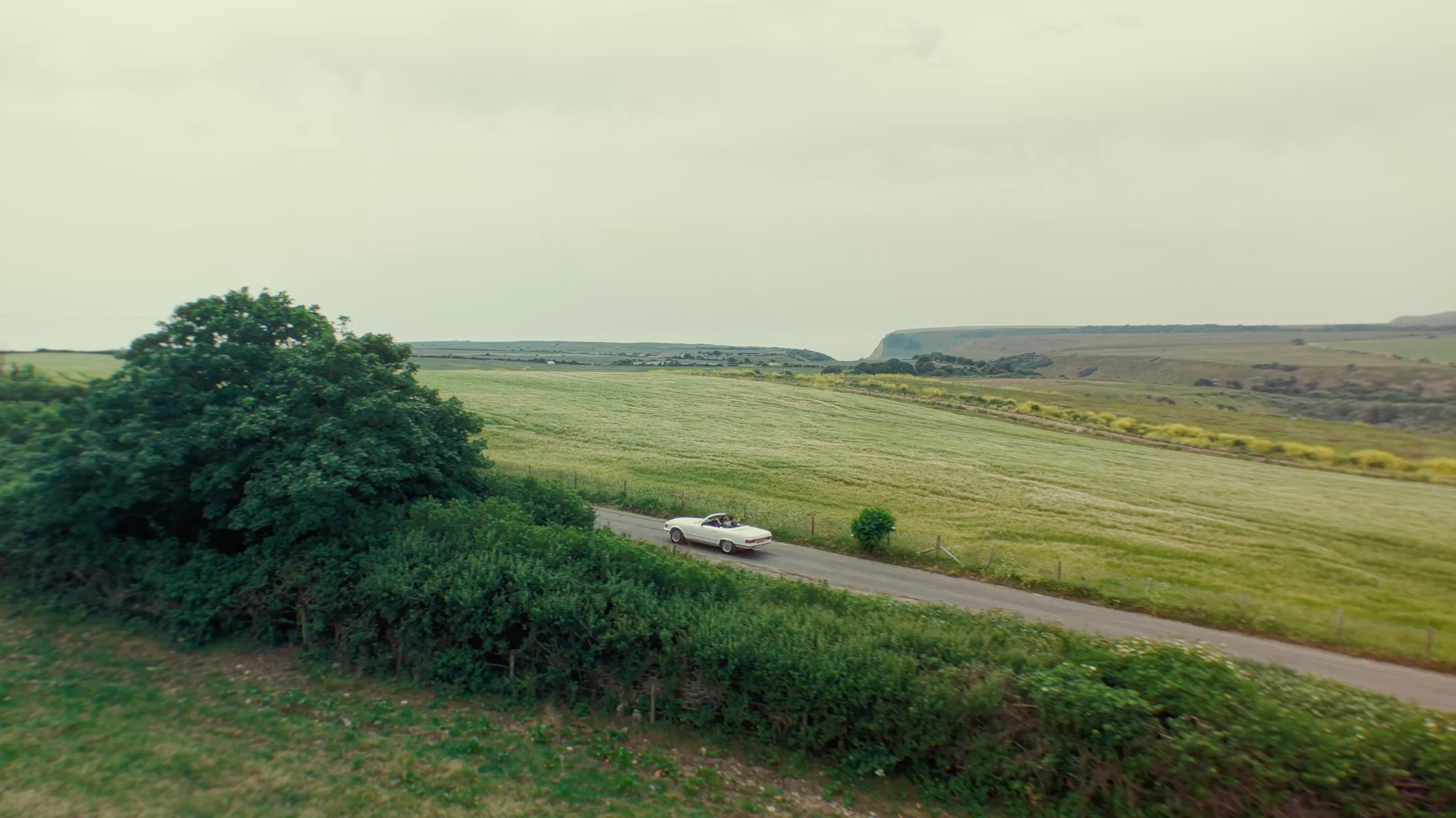 Car driving on a rural road with green fields and hills in the background