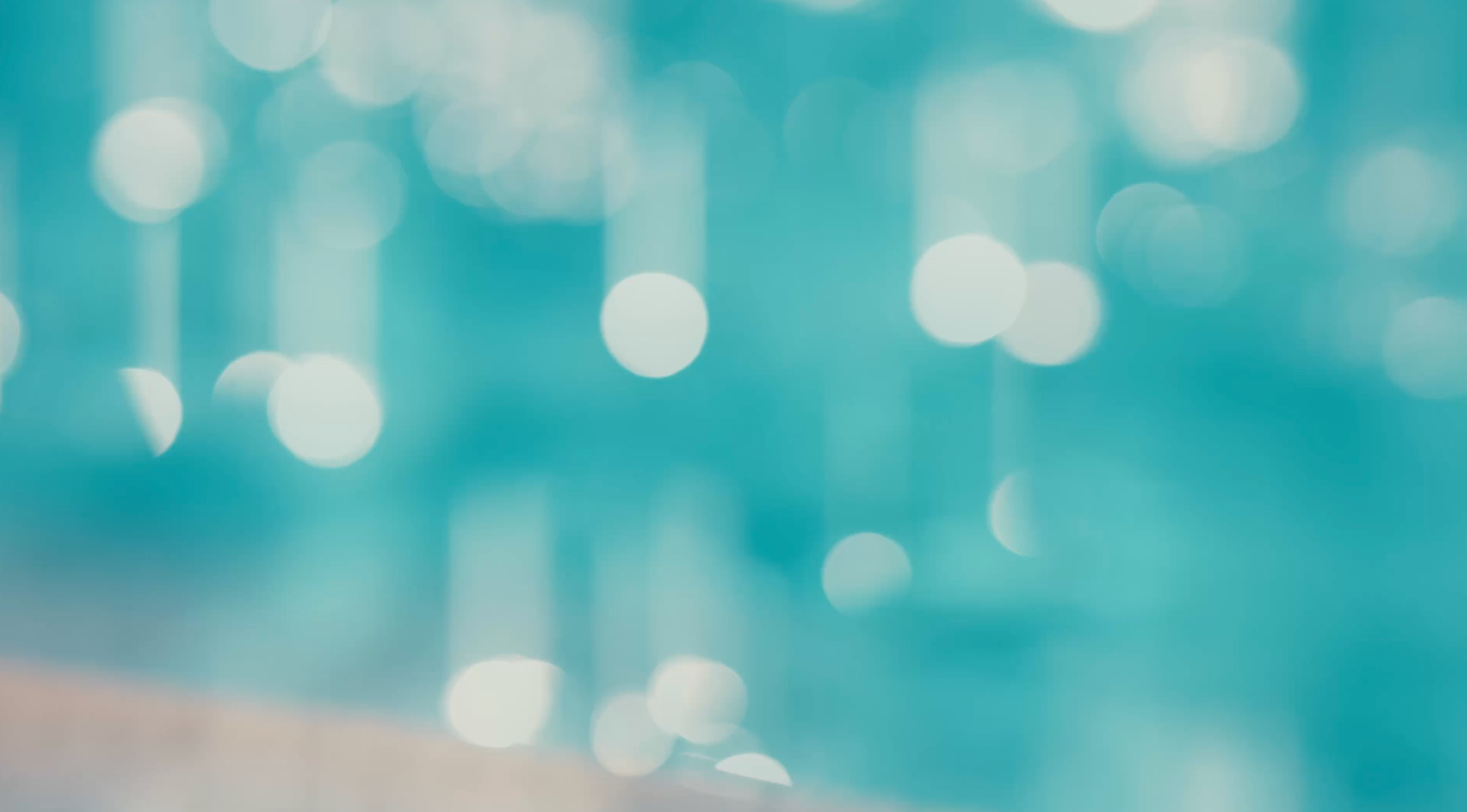A soft, out-of-focus teal and aqua background with white bokeh light circles and a faint warm beige surface at the bottom edge.