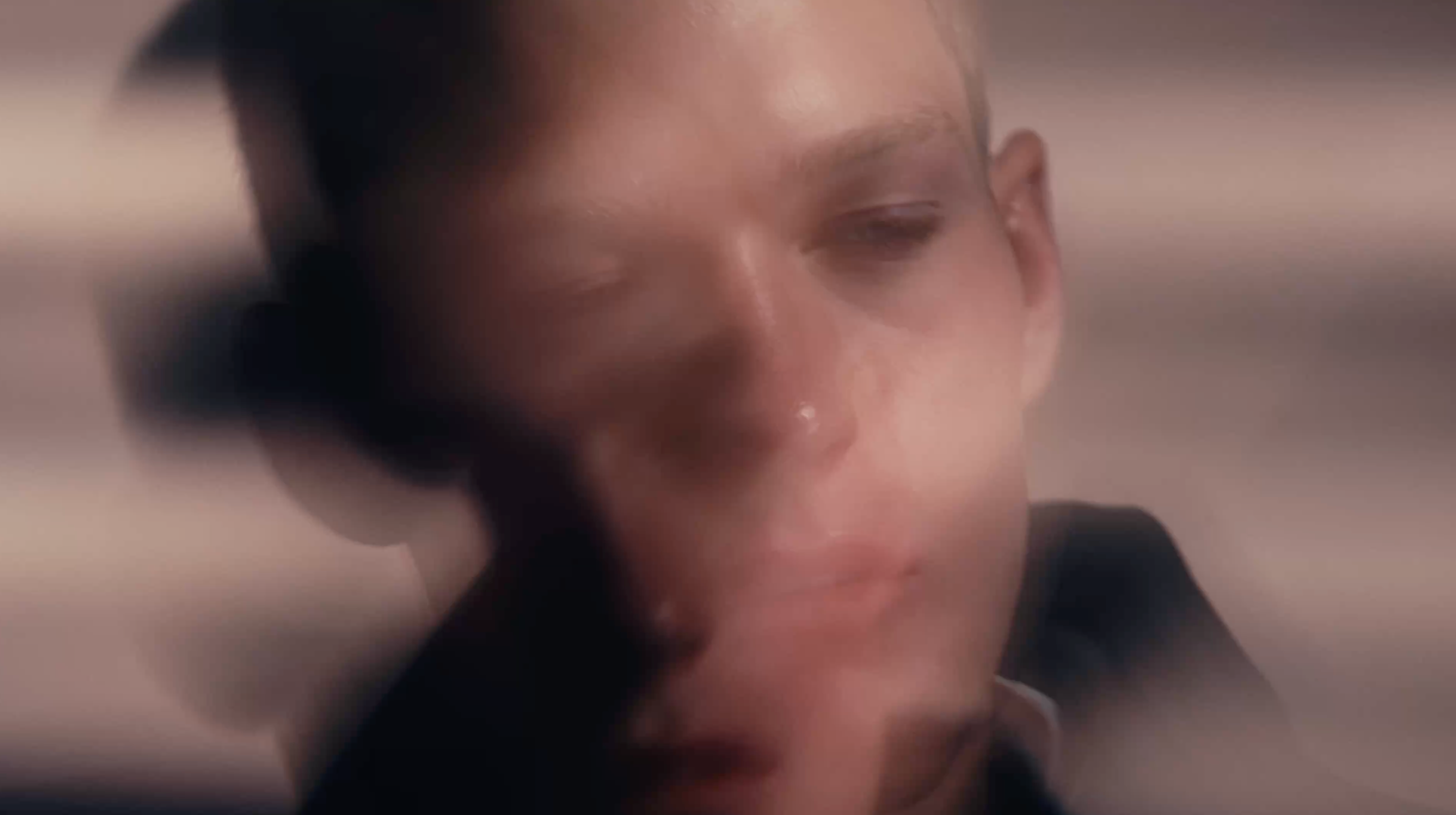 A close-up, heavily blurred portrait of a person's face with soft warm lighting and an abstract, dreamlike quality.
