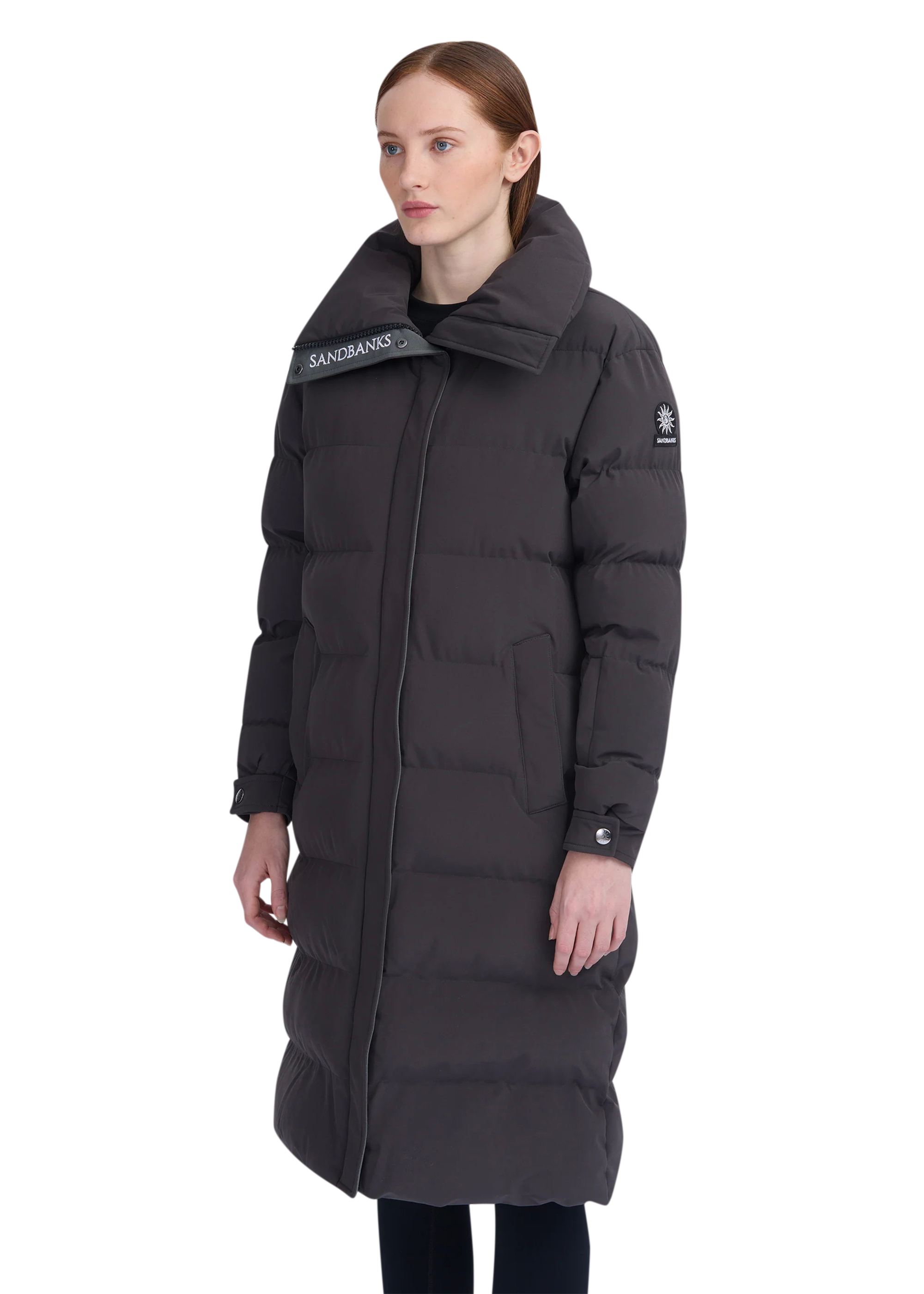 Woman wearing a long black puffer coat with brand logos on a white background