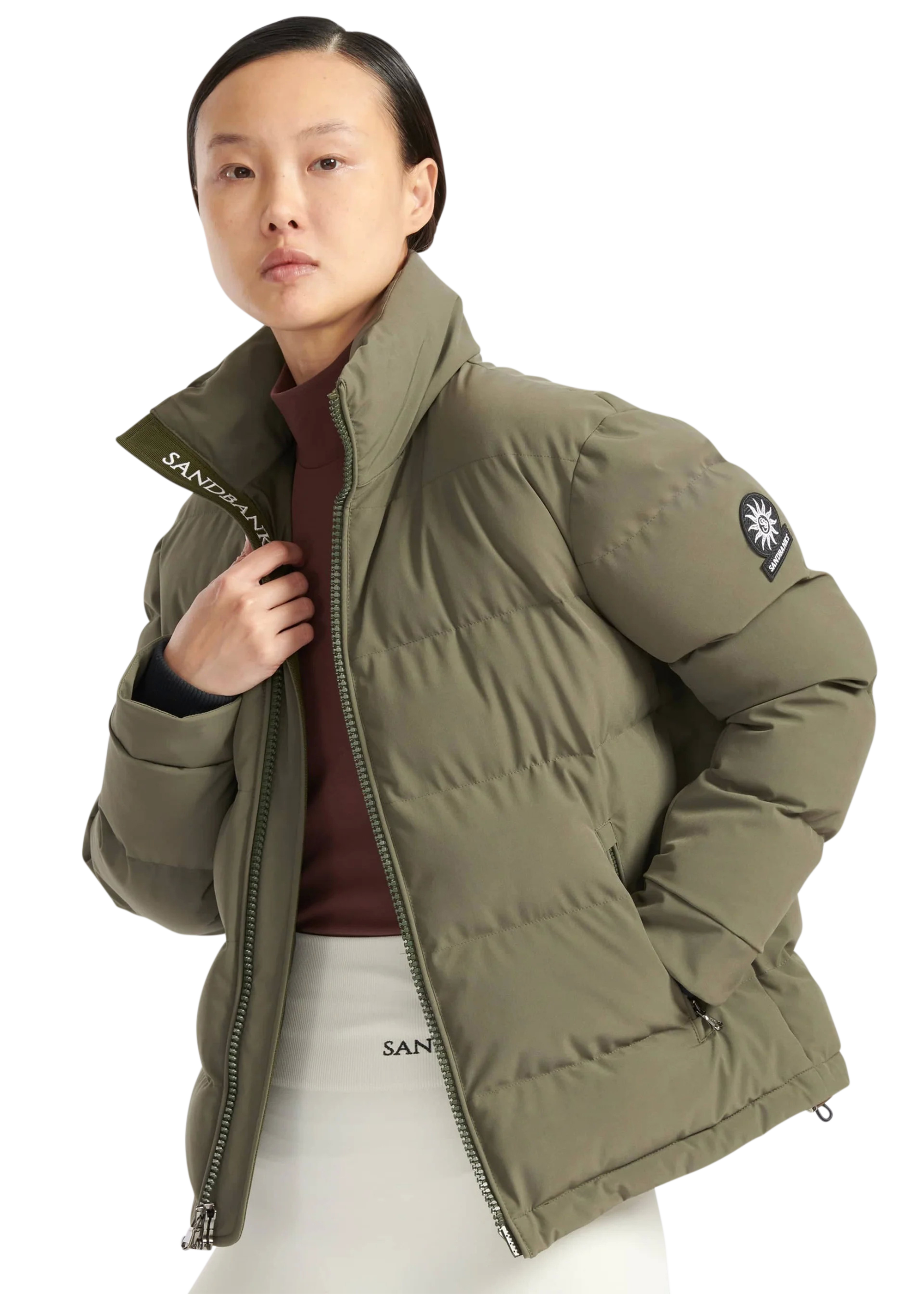 Person wearing a green puffer jacket with a brand logo on a white background