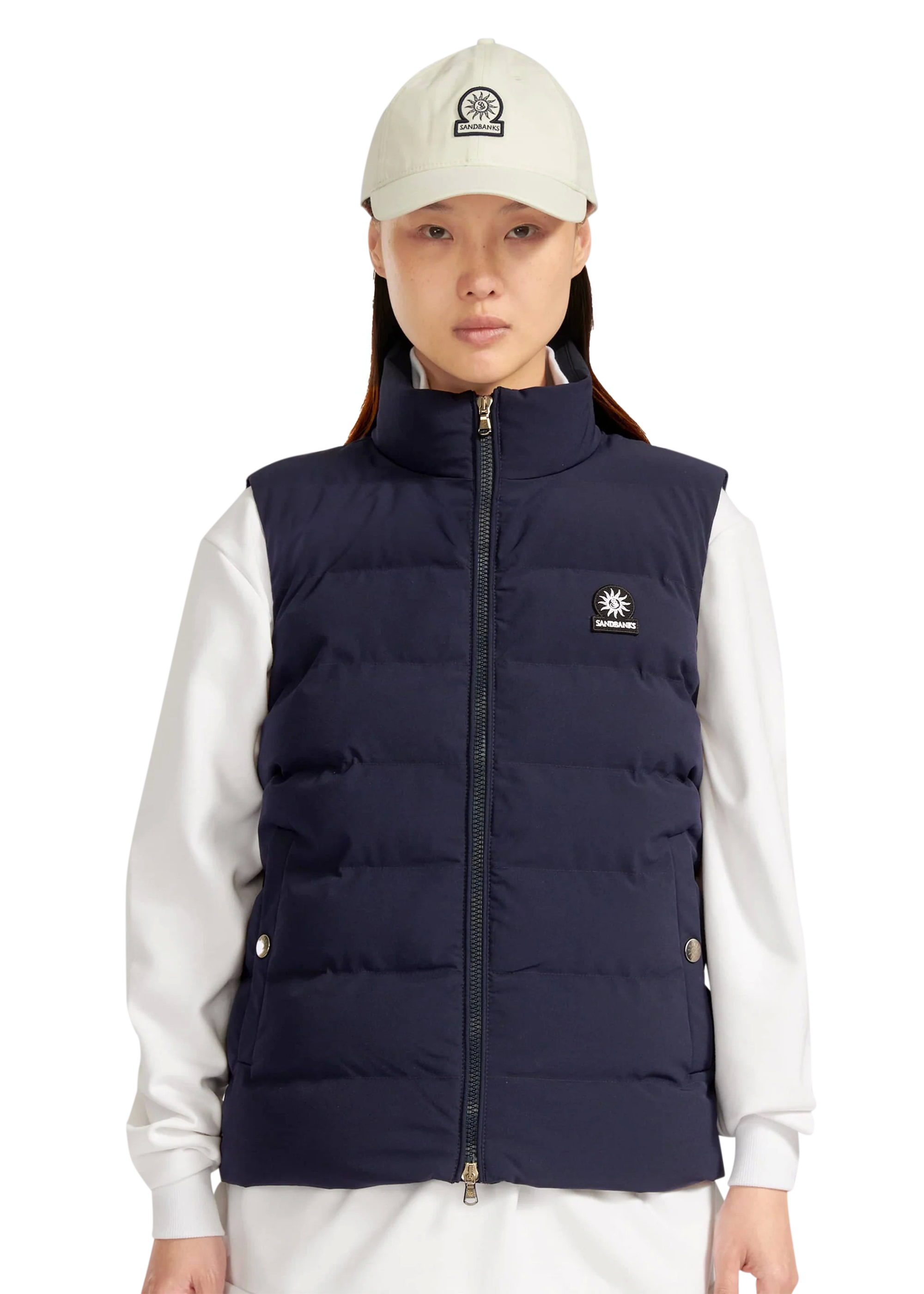 Person wearing a navy puffer vest over a white shirt with a white cap.