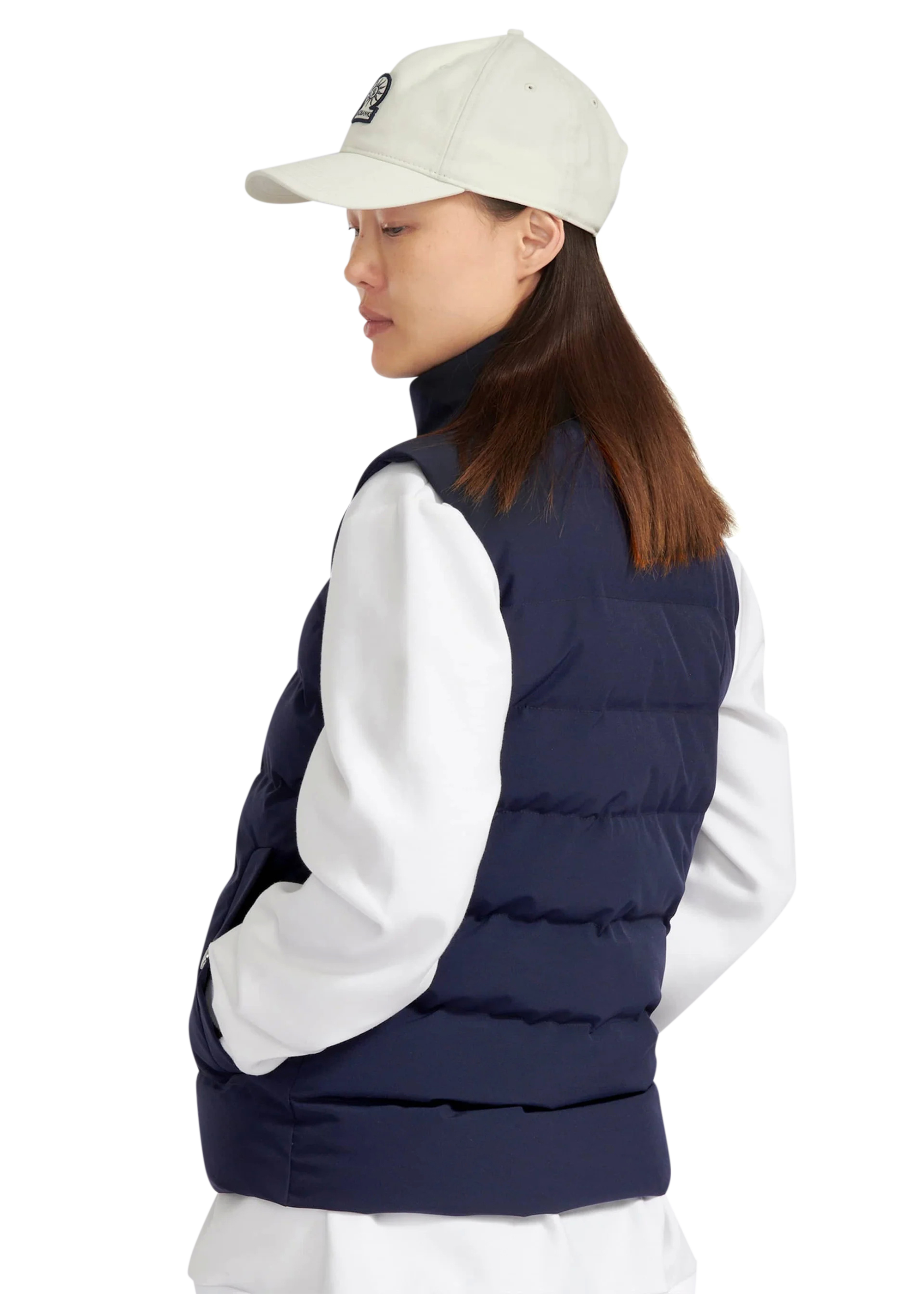 Person wearing a navy puffer vest over a white shirt with a beige cap on a white background