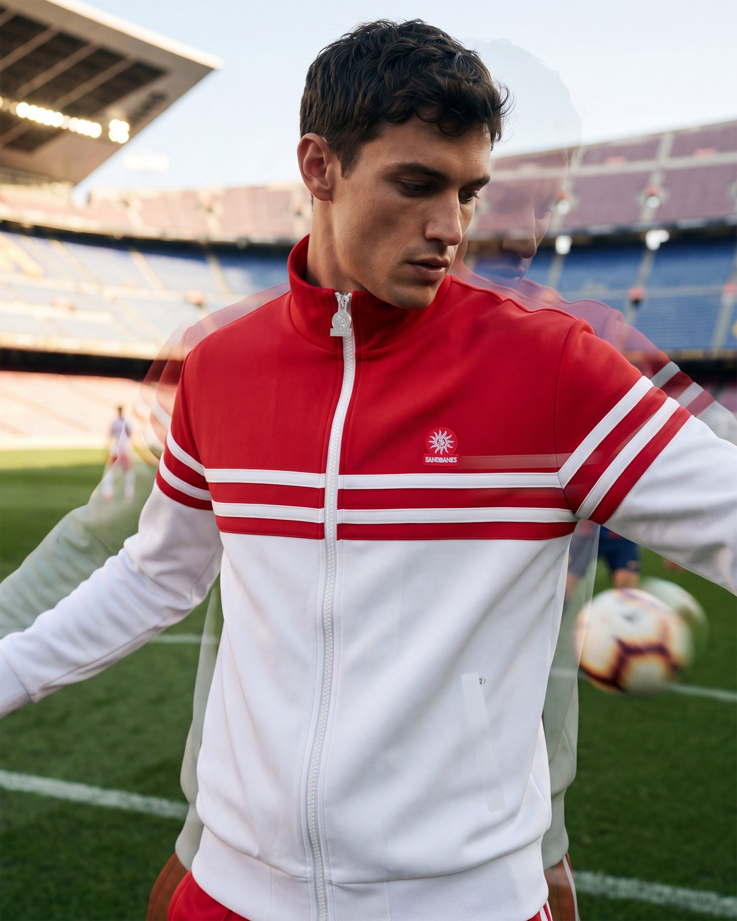 Person wearing a red and white tracksuit with a logo on a sports field.