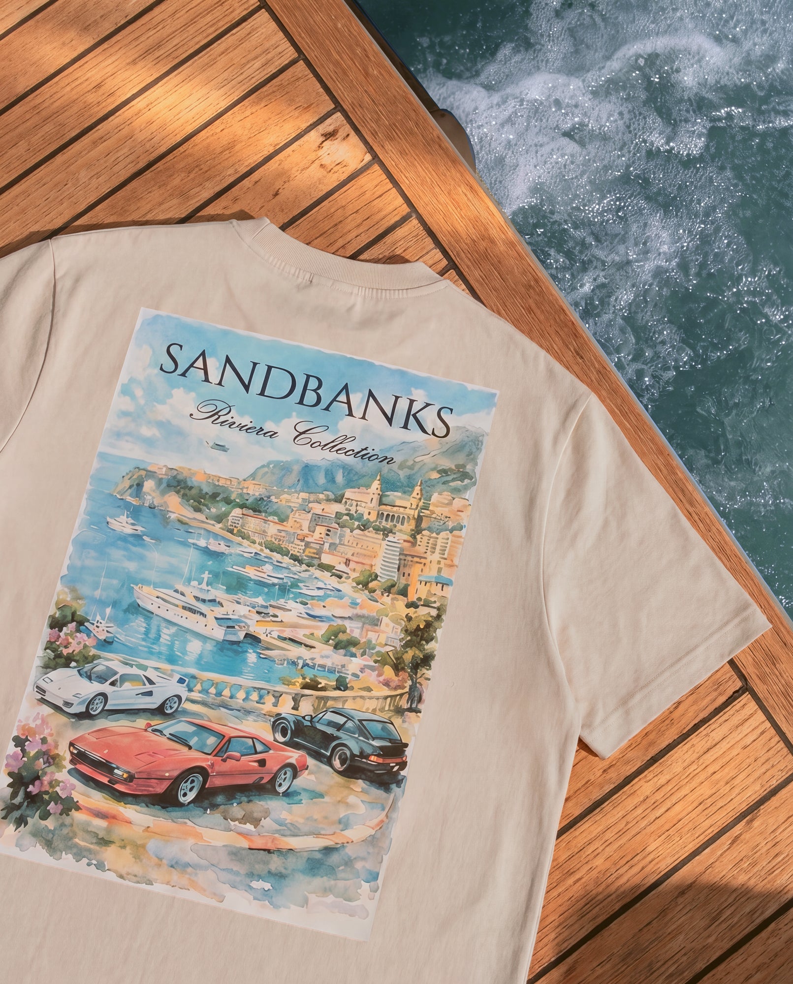 Beige t-shirt with a colorful graphic design of a coastal scene and 'Sandbanks' branding.