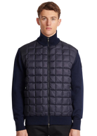 Man wearing a navy puffer vest over a dark blue sweater on a white background